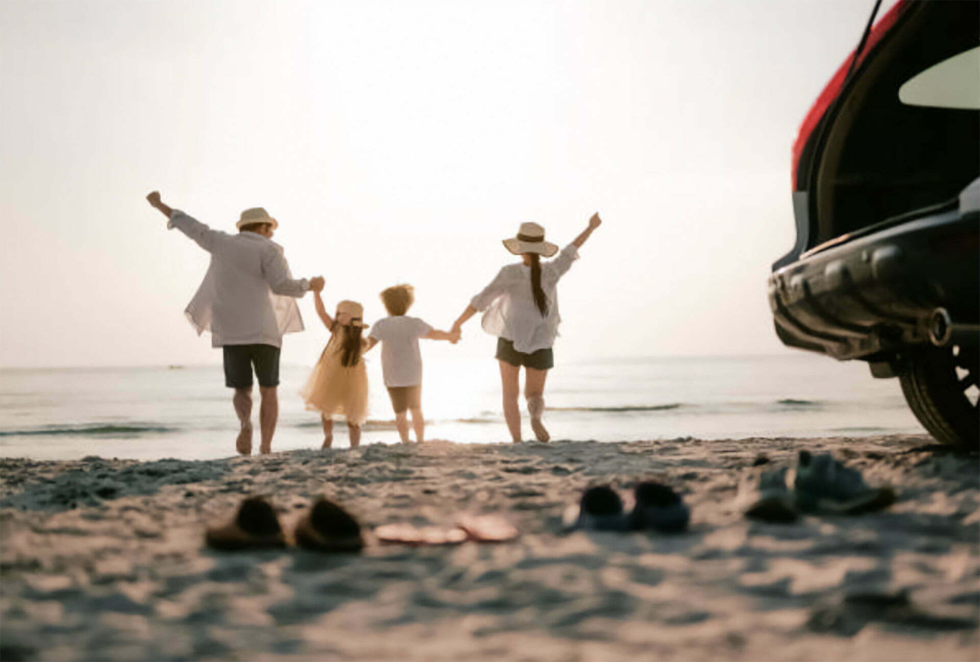 new_hero A family of four holds hands, joyfully walking towards the sea, with their car parked nearby on the sandy beach. The gentle waves seem to wash away worries and bring a sense of freedom as they escape routine like a bird released on bail.
