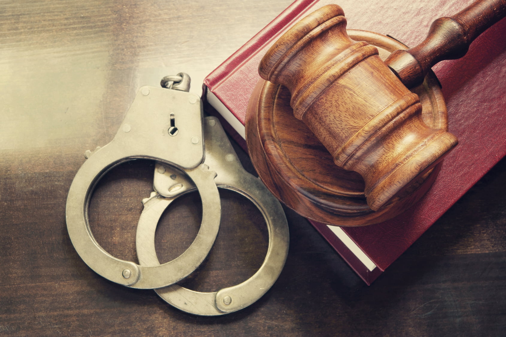 Gavel and handcuffs with red legal book on wooden table A gavel rests on a book beside a pair of handcuffs and an Encinitas Bail Bonds flyer on a wooden surface.