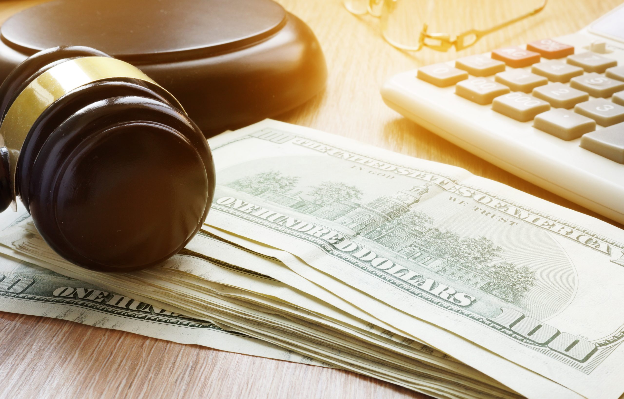 Bail bond concept. Gavel and dollar banknotes. A gavel rests on a stack of hundred-dollar bills beside a calculator, symbolizing the complex financial considerations in California's bail system.