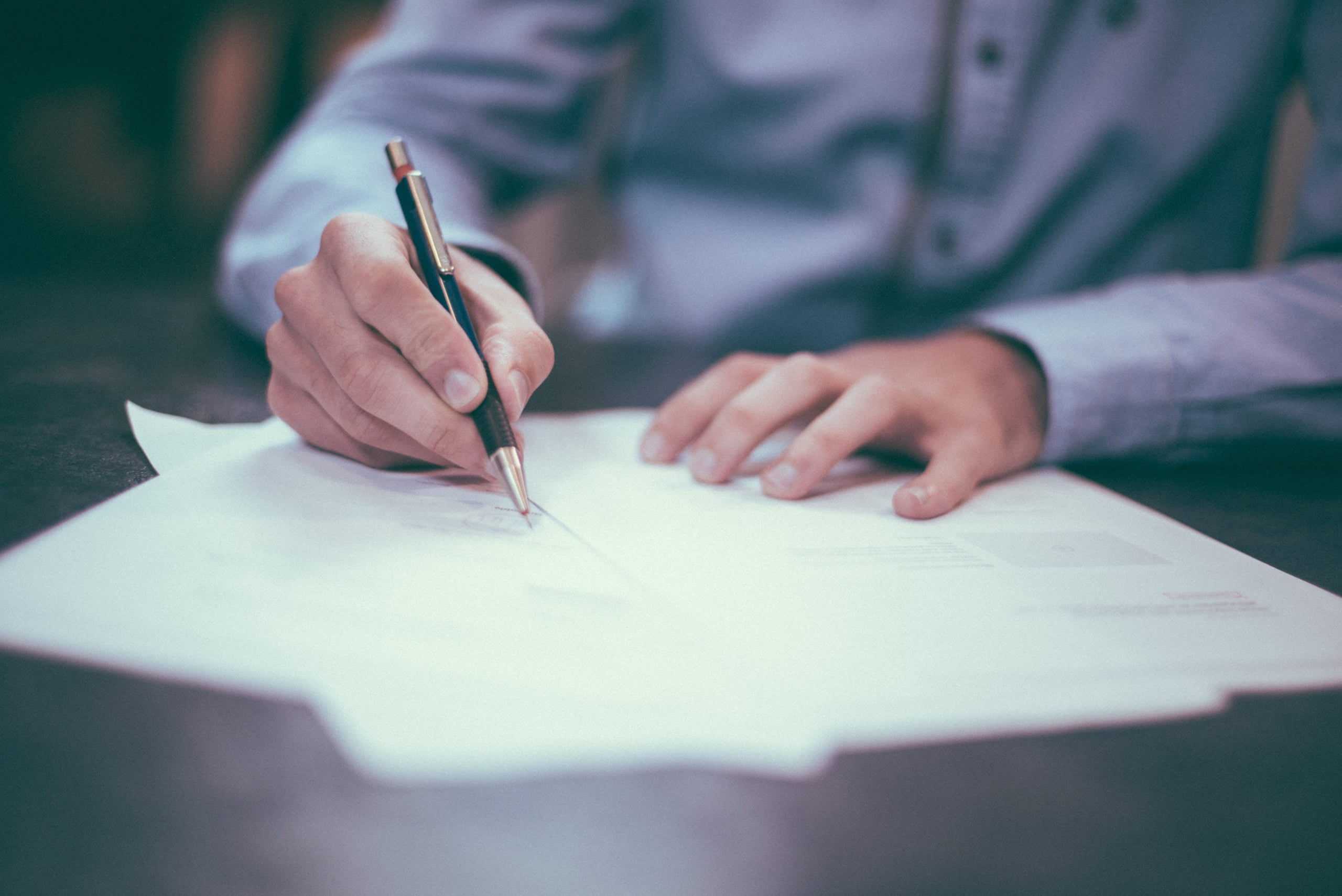 helloquence-51716-unsplash A person in a blue shirt is meticulously writing with a pen on white papers at a desk, possibly drafting documents related to California bail bonds.