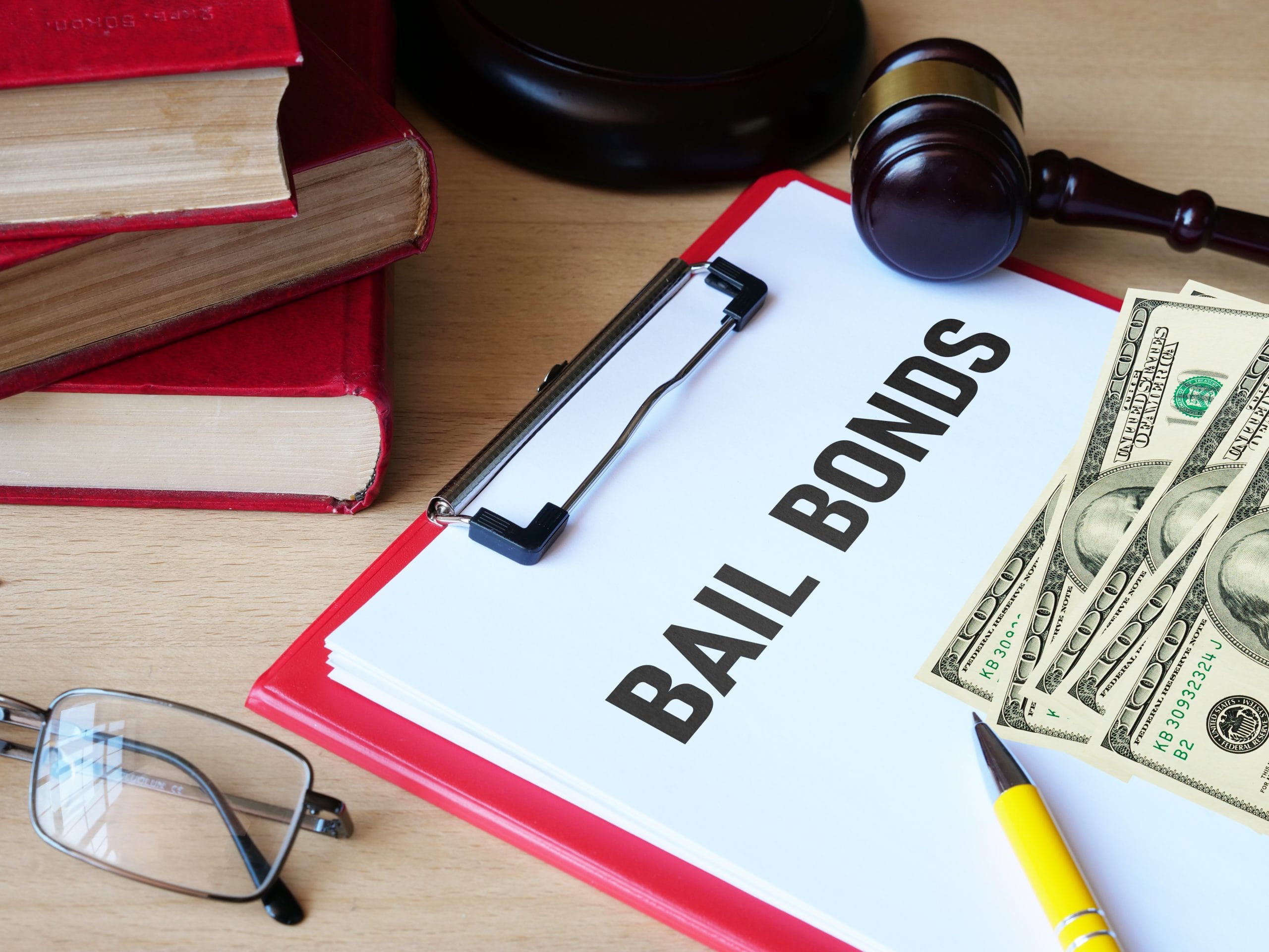 Bail bonds are shown using the text A clipboard labeled "Bail Bonds" with cash, gavel, books, glasses, and a yellow pen on a desk.